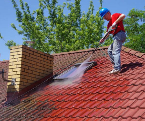 House roof cleaning with pressure tool. Worker on top of building washing tile with professional equipment. Moss removing with water.