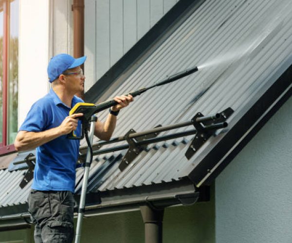 man standing on ladder and cleaning house metal roof with high pressure washer