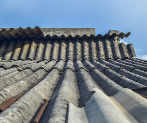 side view of asbestos or top cover of a weathered old building against the background of a blue sky with white clouds on a sunny day