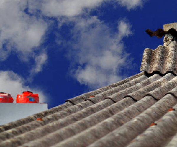 old asbestos roofed building. side view of asbestos or weathered building top covering against bright daytime sky background . the building with the two water storage tanks looks blur