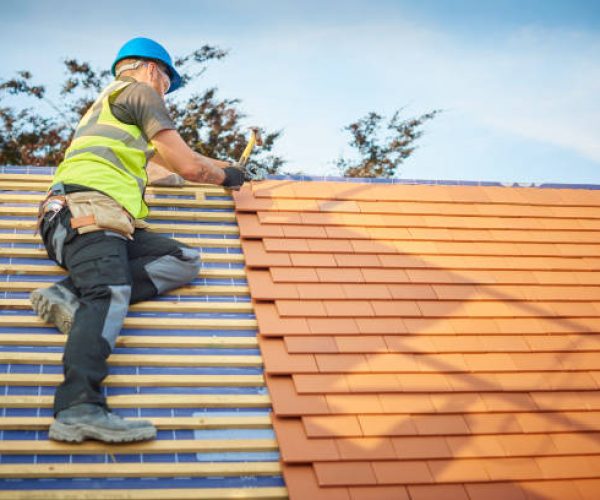 a roofer nails on the roof tiles