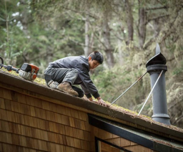 Man cleaning rain gutters on roof with blower