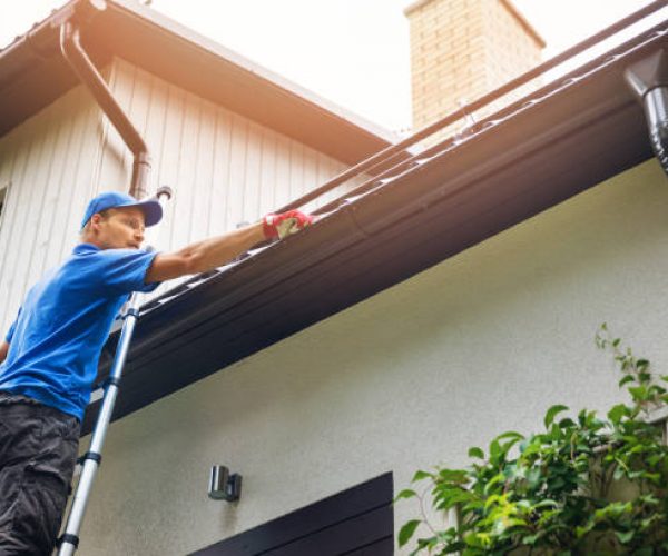man on ladder cleaning house gutter from leaves and dirt