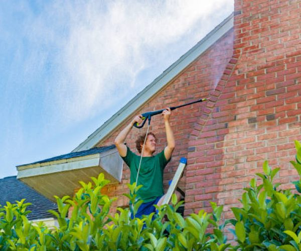 A young man cleans a red brick house exterior.
