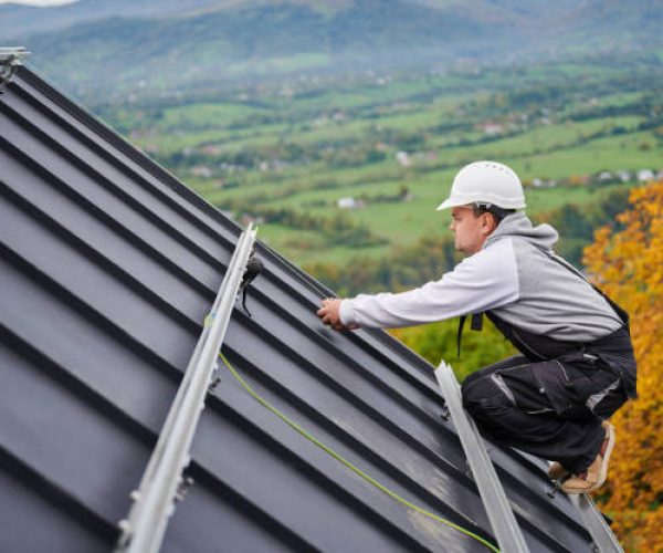 Man roofer prepearing for mounting photovoltaic solar modules on roof of house. Electrician in helmet installing solar panel system outdoors. Concept of alternative and renewable energy.
